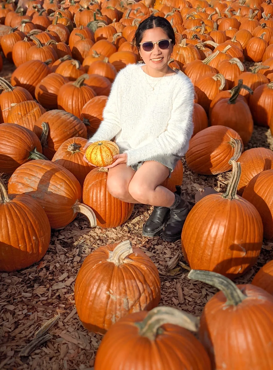 Pumpkin patch outfit ideas shown by a woman in casual fall clothes among pumpkins