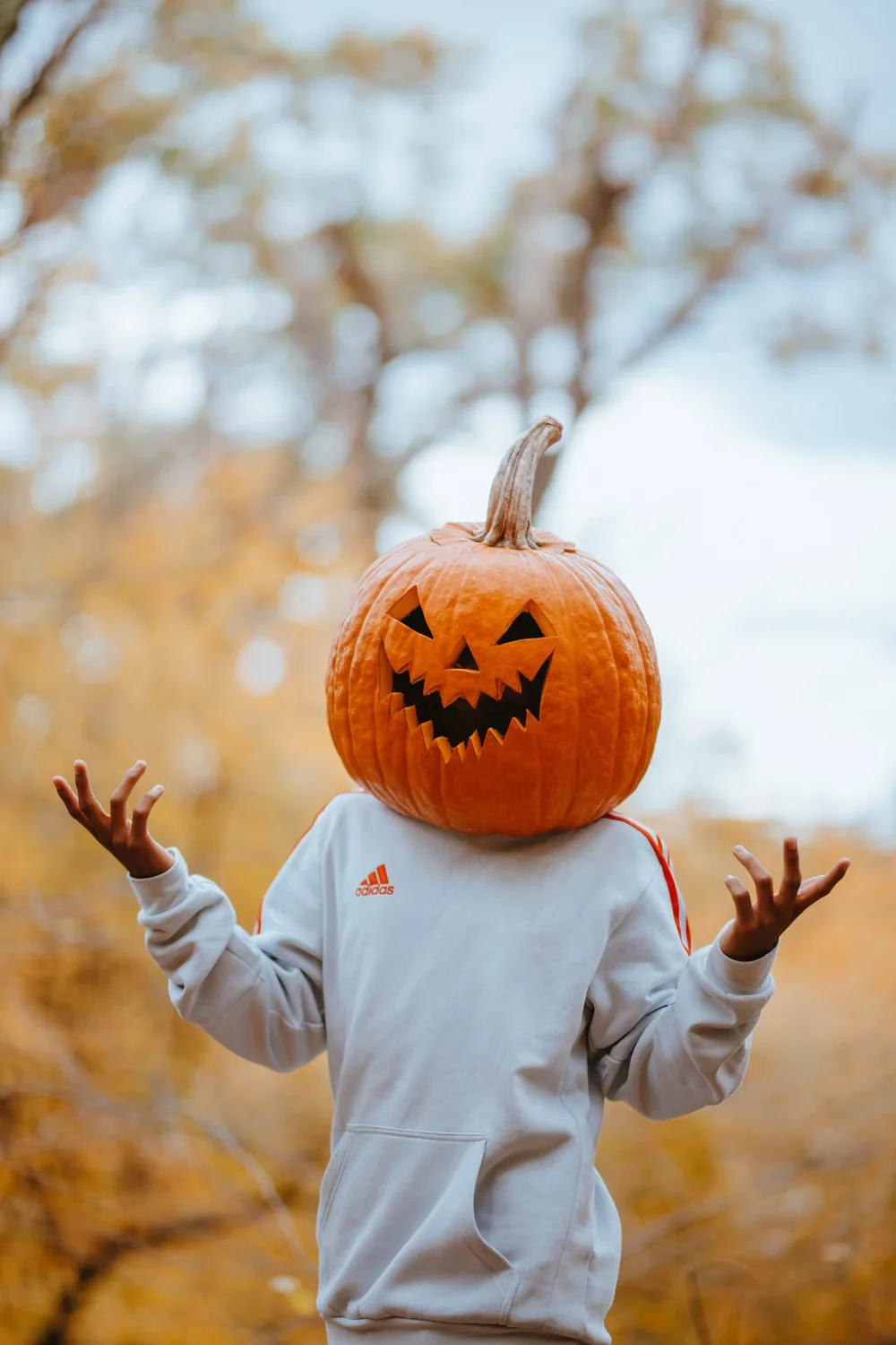 Summerween outfit ideas with a white hoodie and pumpkin head in an autumn forest