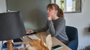 Woman in a gray sweatshirt working at a computer in a home office