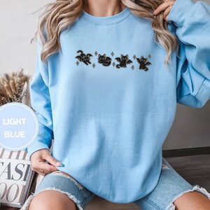 Person wearing a light blue Bat Wing Cats Embroidered Sweatshirt