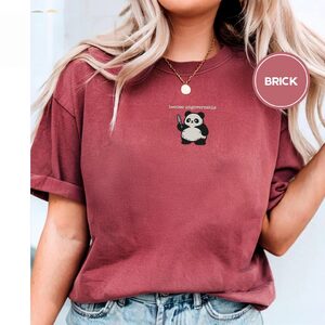 Person wearing a brick Become Ungovernable Panda Embroidered T-Shirt