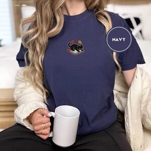 Person wearing a navy Black Cat on Book Embroidered T-Shirt