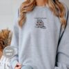 Person wearing a sport grey Bookish Raccoon Embroidered Sweatshirt