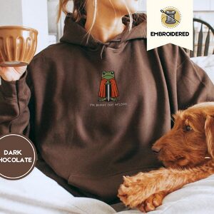 Person wearing a dark chocolate Burnt Out Frog Knight Embroidered Hoodie