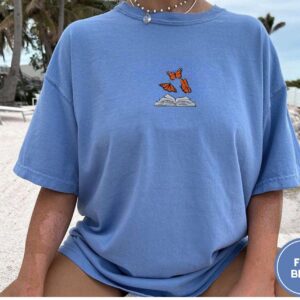 Person wearing a flo blue Butterflies and Open Book Embroidered T-Shirt
