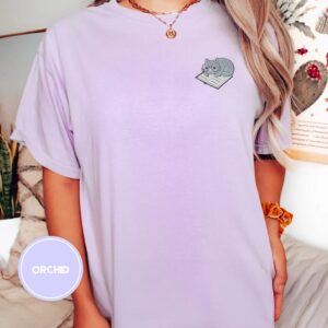 Person wearing an orchid Cat on Open Book Embroidered T-Shirt