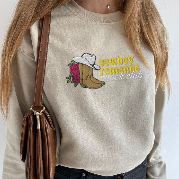 Person wearing a sand Cowboy Romance Book Club Embroidered Sweatshirt