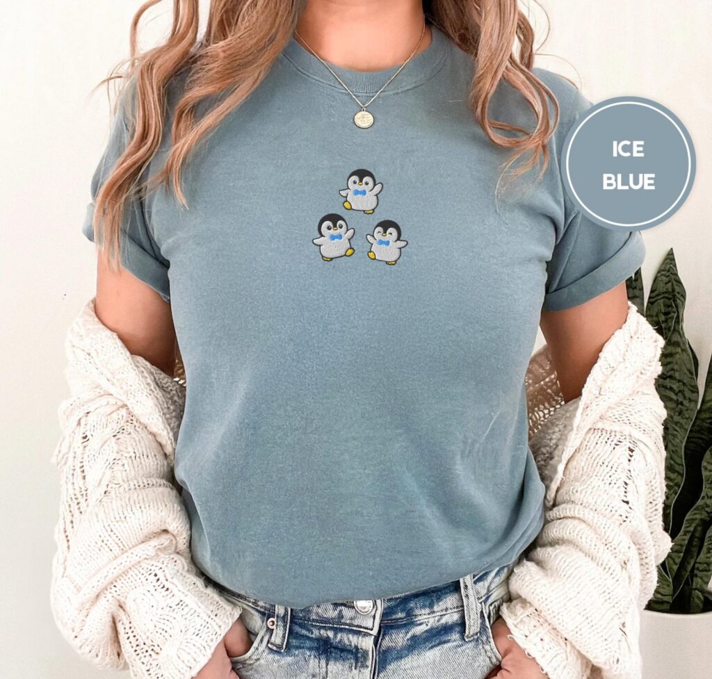 Person wearing an ice blue Dancing Penguins Embroidered T-Shirt
