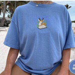 Person wearing a flo blue Deer and Open Book Embroidered T-Shirt