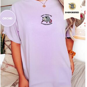 Person wearing an orchid Don't Touch Me Possum Embroidered T-Shirt
