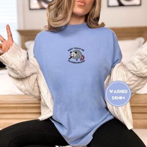 Person wearing a washed denim Don't Touch Me Possum Embroidered T-Shirt