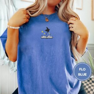 Person wearing a flo blue Dragon and Open Book Embroidered T-Shirt