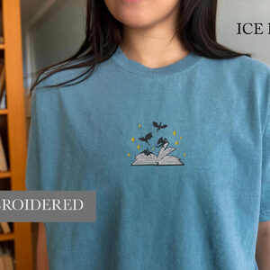 Person wearing an ice blue Dragons and Open Book Embroidered T-Shirt
