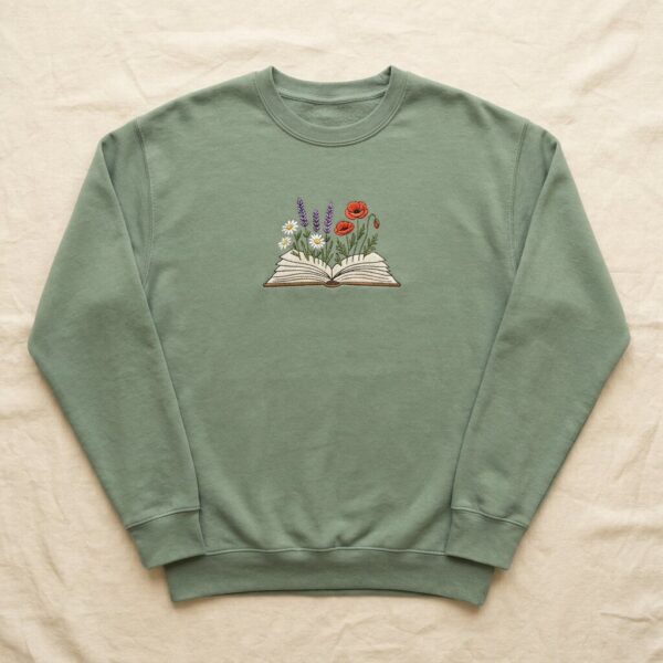 Sage green sweatshirt with an embroidered open book growing daisies, lavender and poppies