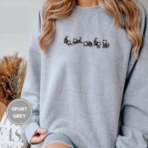 Person wearing a sport grey Five Skeleton Cat Poses Embroidered Sweatshirt