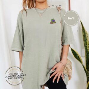 Person wearing a bay Frog Reading On A Log Embroidered T-Shirt