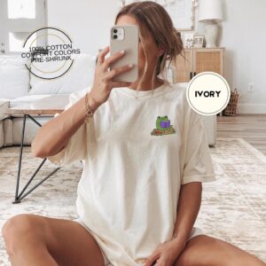 Person wearing an ivory Frog Reading On A Log Embroidered T-Shirt