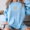 Person wearing a light blue Gold Read Banned Books Embroidered Sweatshirt