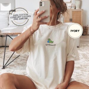 Person wearing an ivory Green Worm Blue Book Embroidered T-Shirt