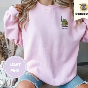Person wearing a light pink Huzzah Frog Knight Embroidered Sweatshirt