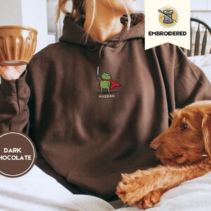 Person wearing a dark chocolate Huzzah Knight Frog Embroidered Hoodie