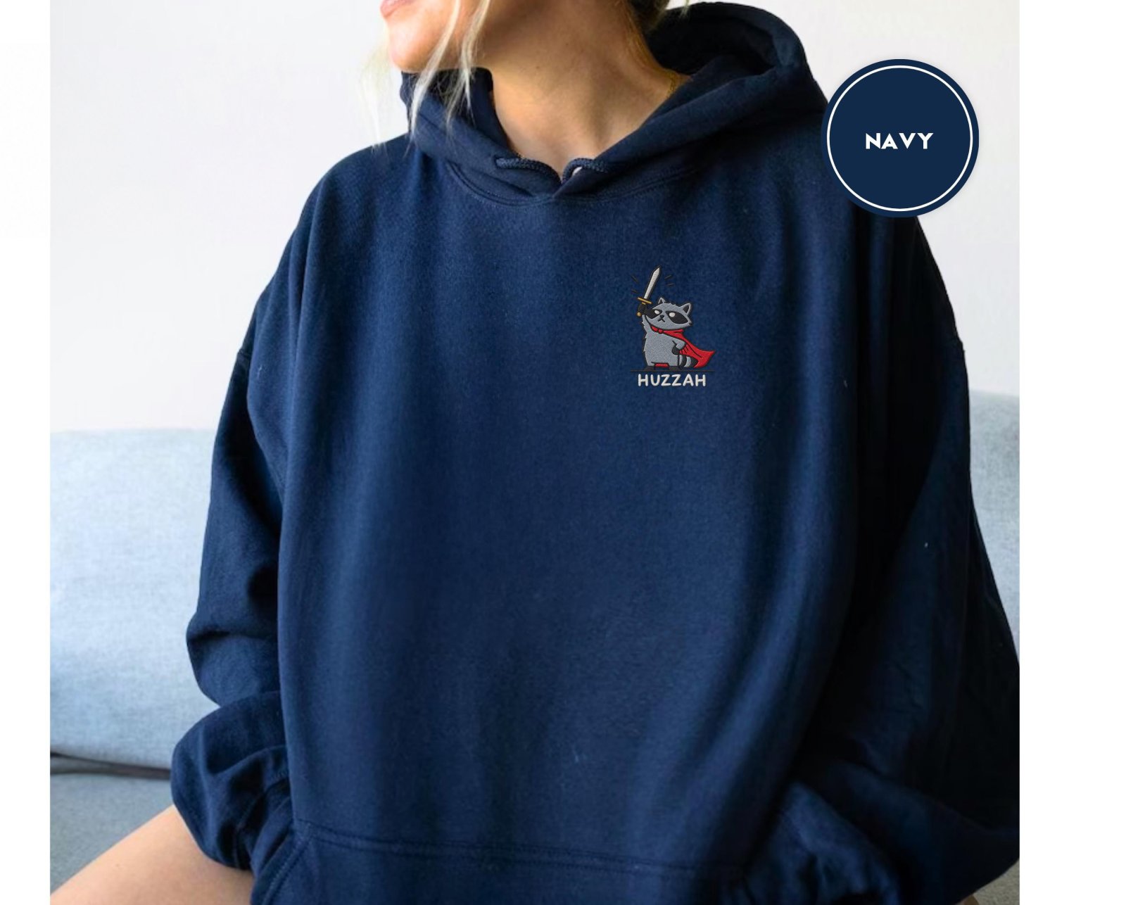 Person wearing a navy Huzzah Raccoon Knight Embroidered Hoodie