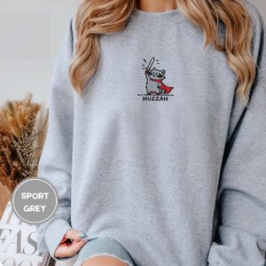 Person wearing a sport grey Huzzah Raccoon Knight Embroidered Sweatshirt