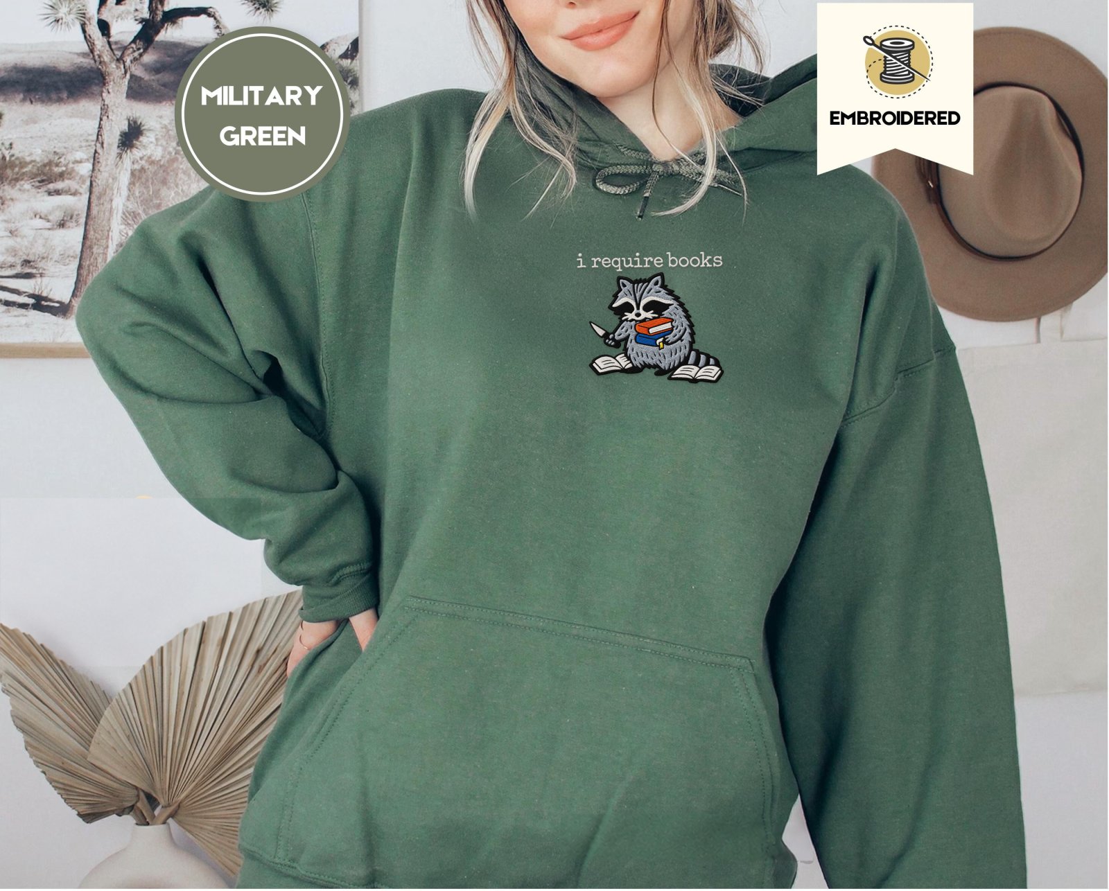 Person wearing a military green I Require Books Raccoon Embroidered Hoodie