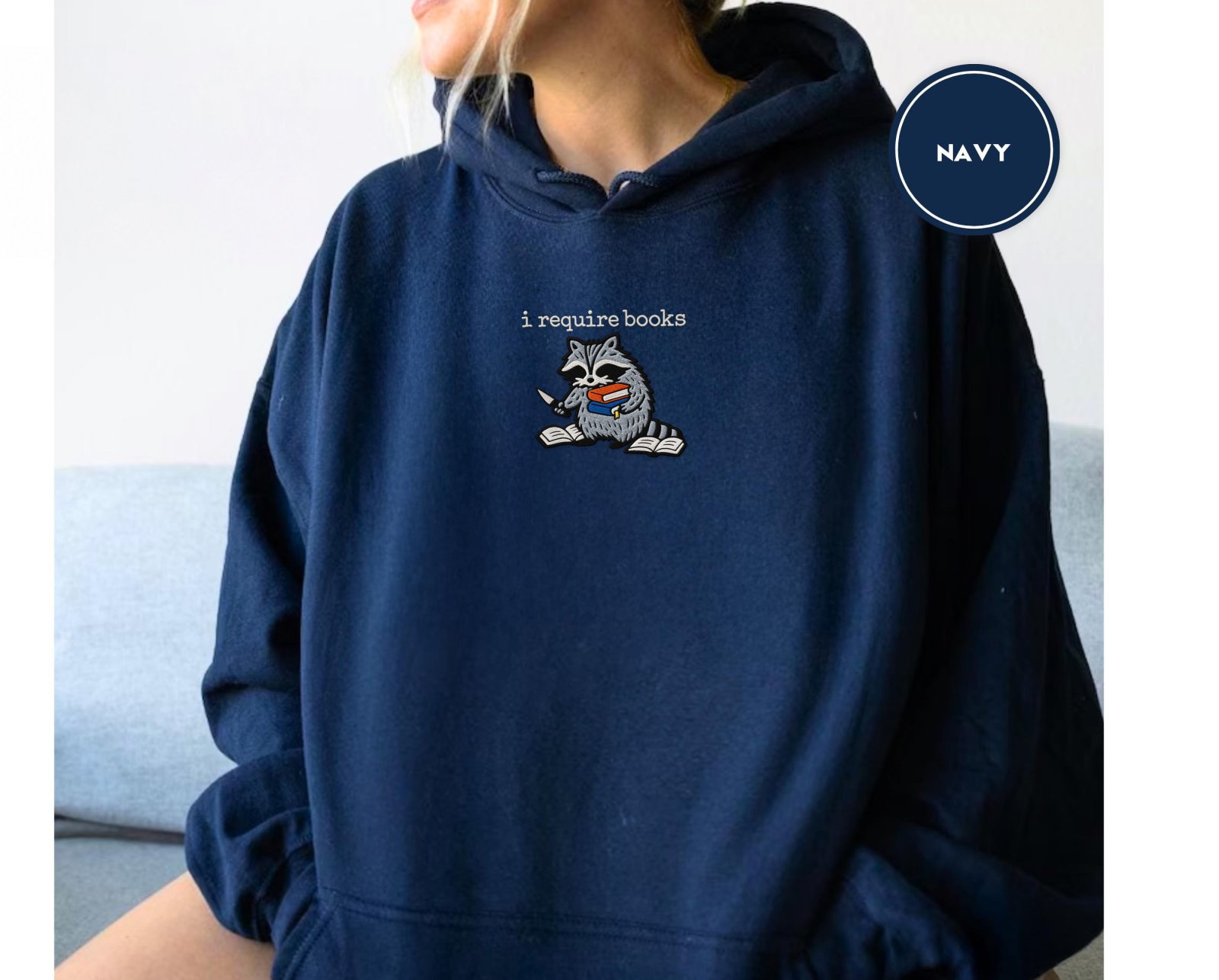 Person wearing a navy I Require Books Raccoon Embroidered Hoodie