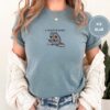 Person wearing an ice blue I Require Books Raccoon Embroidered T-Shirt