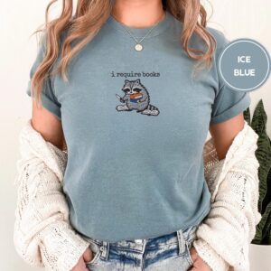 Person wearing an ice blue I Require Books Raccoon Embroidered T-Shirt