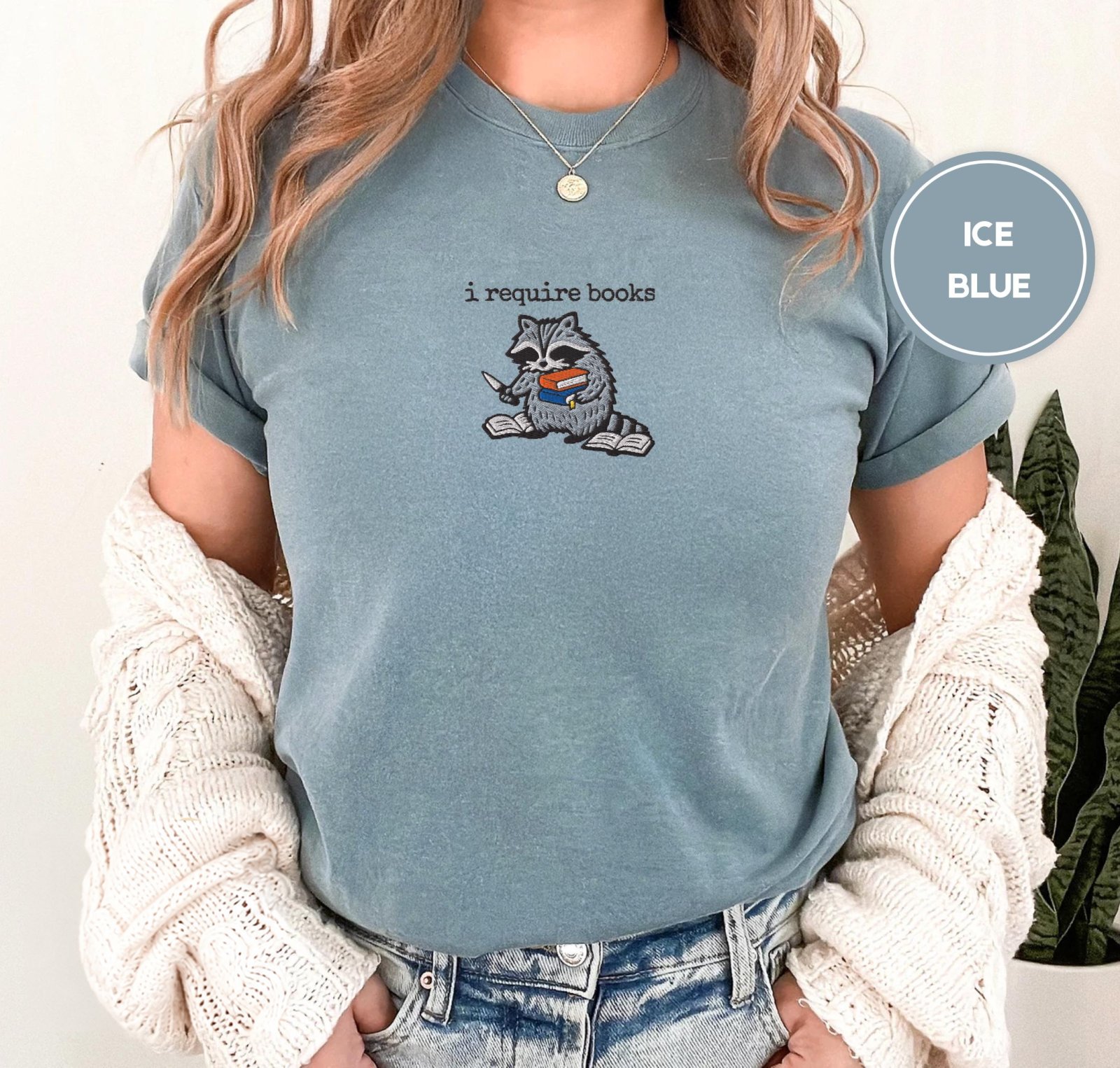 Person wearing an ice blue I Require Books Raccoon Embroidered T-Shirt