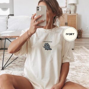 Person wearing an ivory I Require Snacks Raccoon Embroidered T-Shirt