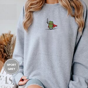 Person wearing a sport grey Knight Frog Embroidered Sweatshirt