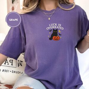Person wearing a grape Luck Is Overrated Black Cat Embroidered T-Shirt