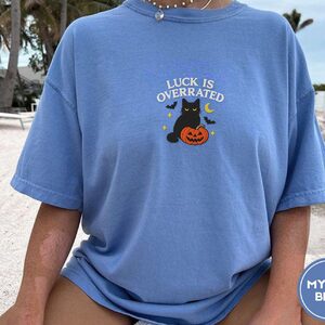 Person wearing a mystic blue Luck Is Overrated Black Cat Embroidered T-Shirt