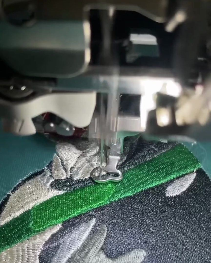 Close-up of an embroidery machine needle and presser foot stitching a cow design onto green fabric held in a hoop
