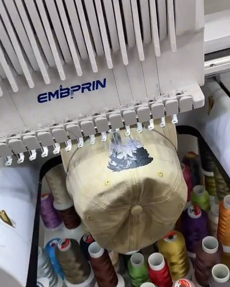 Multi-needle embroidery machine stitching a design, with thread cones in many colors below it