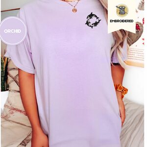 Person wearing an orchid Orca Whales Embroidered T-Shirt