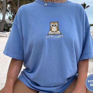 Person wearing a mystic blue Owl Be Reading Embroidered T-Shirt