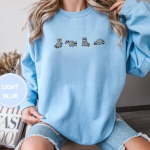Person wearing a light blue Playful Raccoons Embroidered Sweatshirt