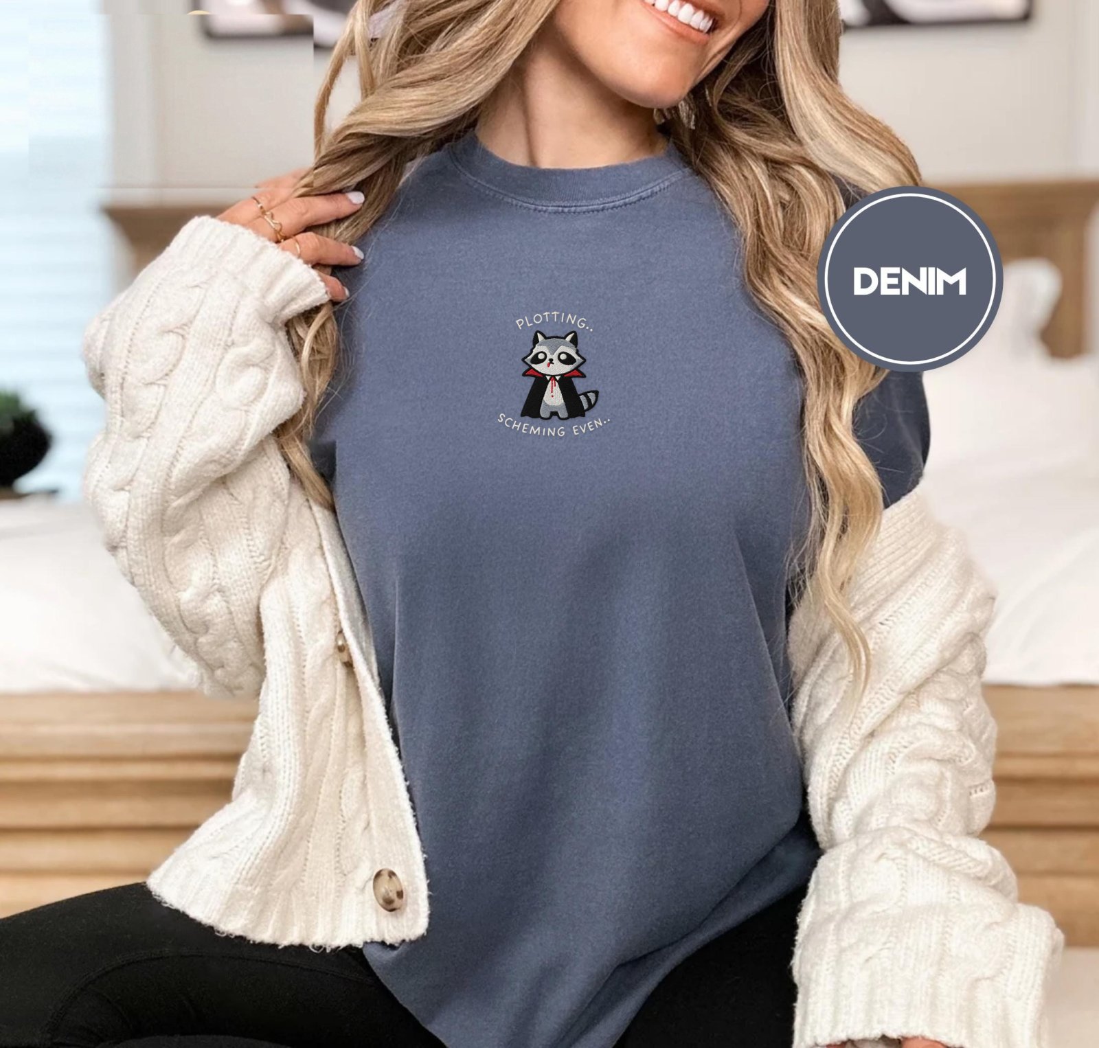 Person wearing a denim Plotting Vampire Raccoon Embroidered T-Shirt