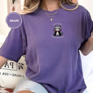Person wearing a grape Plotting Vampire Raccoon Embroidered T-Shirt
