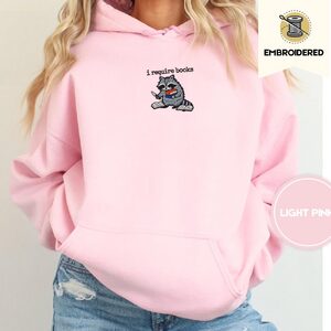 Person wearing a light pink Raccoon and Open Books Embroidered Hoodie