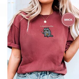 Person wearing a brick Raccoon With Knife and Mug Embroidered T-Shirt