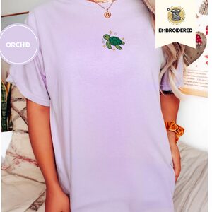 Person wearing an orchid Sea Turtle and Sparkles Embroidered T-Shirt