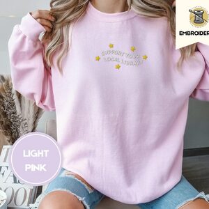 Person wearing a light pink Support Your Local Library Embroidered Sweatshirt