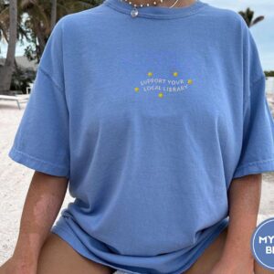 Person wearing a mystic blue Support Your Local Library Embroidered T-Shirt