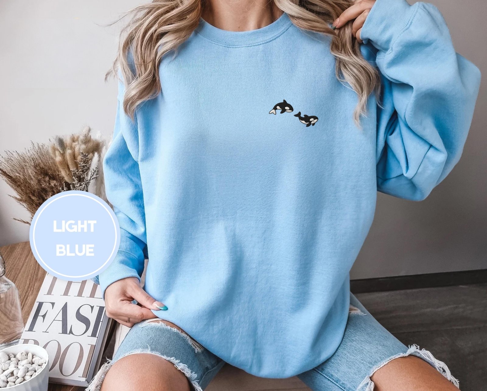 Person wearing a light blue Swimming Orcas Embroidered Sweatshirt
