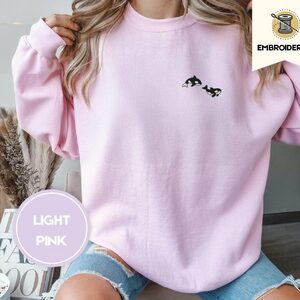 Person wearing a light pink Swimming Orcas Embroidered Sweatshirt